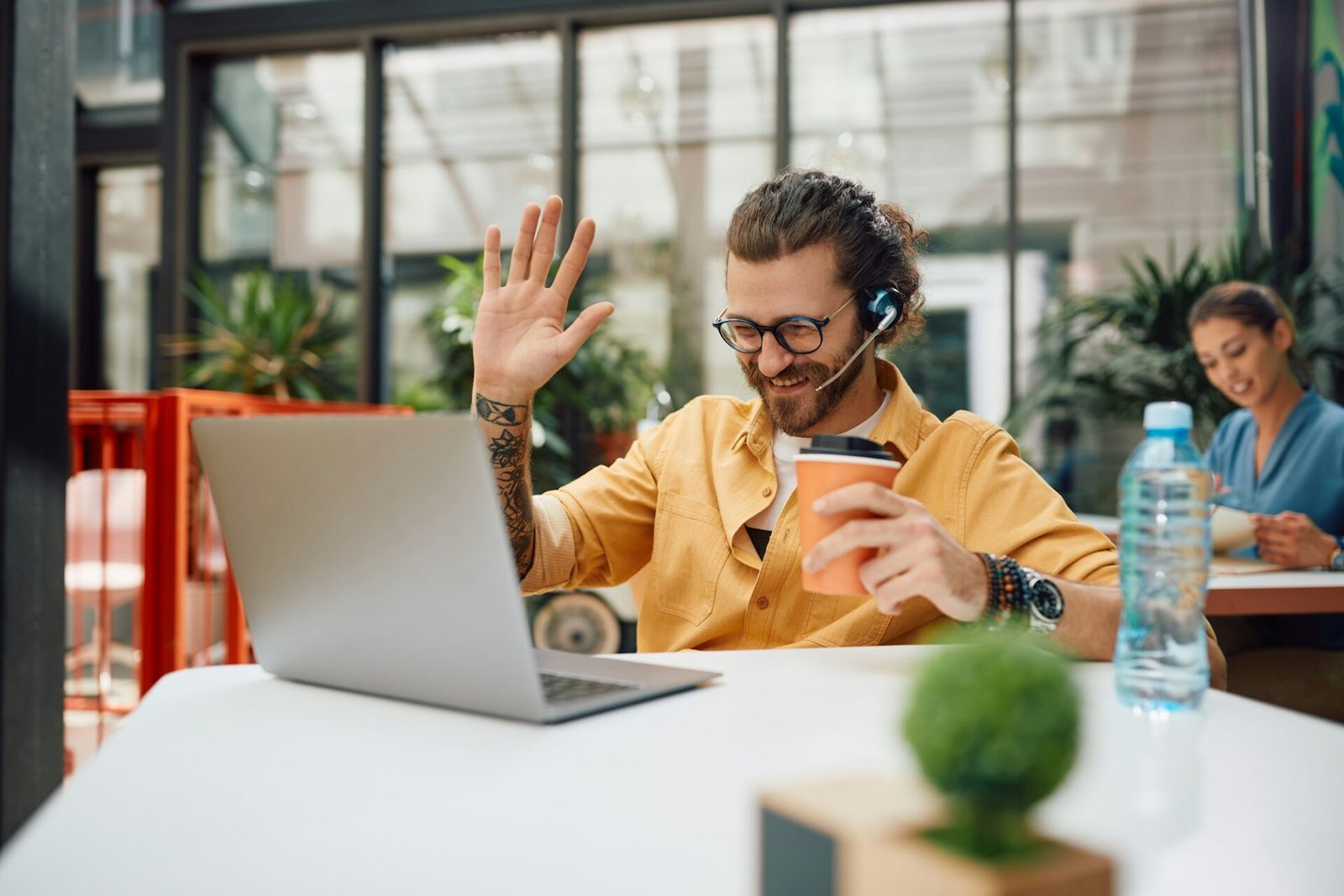 Happy freelancer greeting someone during video call on his coffee break in a cafe.